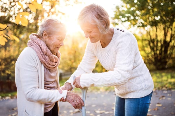 Two elderly women assisting each other outdoors in autumn.