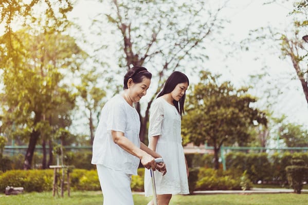 An older woman with a cane walking with a younger woman in a garden.
