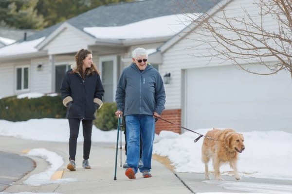 Senior resident walking a dog with a staff member outside