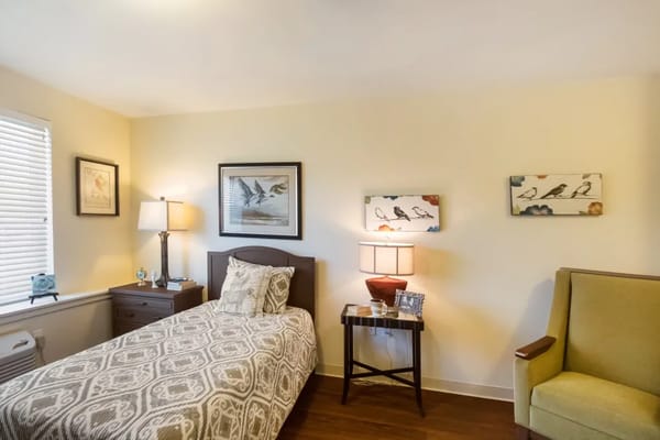 A cozy bedroom with a single bed, lamp, and artwork.