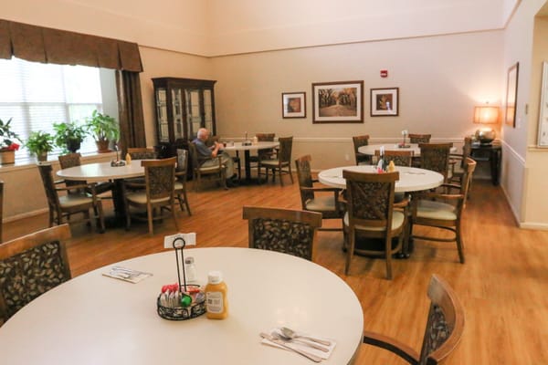 Spacious dining room with round tables and an elderly resident enjoying a meal