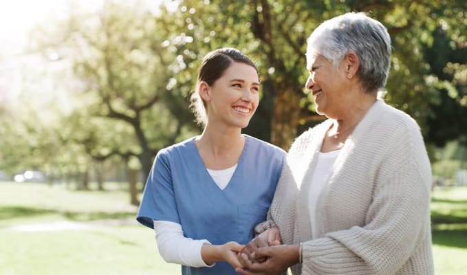 Caregiver and senior resident smiling while holding hands in a park.