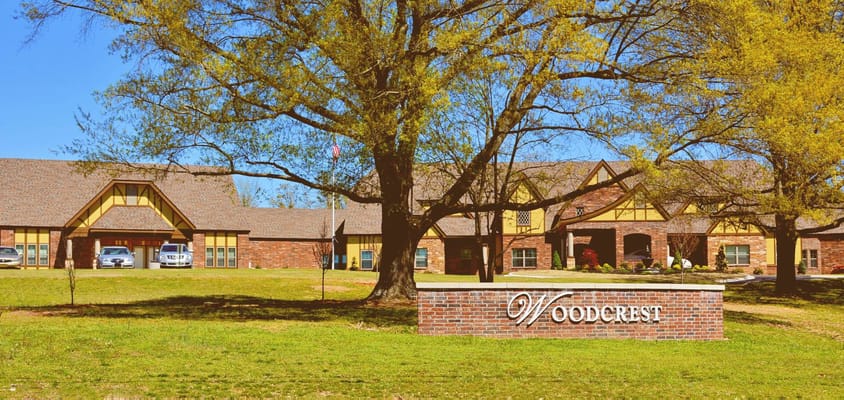 Front view of Woodcrest Assisted Living facility with sign and trees.