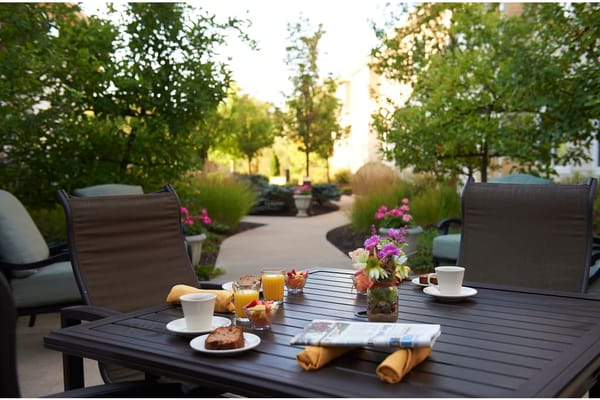 A table set for breakfast outdoors, featuring beverages, food, and flowers.