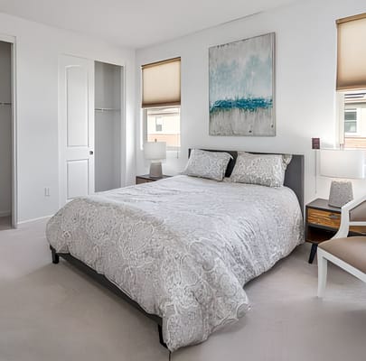 A well-furnished bedroom with a queen-sized bed, abstract artwork on the wall, and natural light.