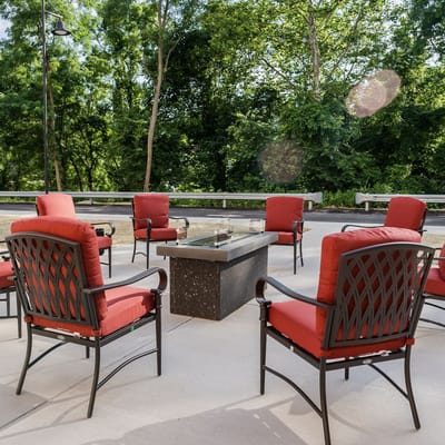 Outdoor seating area with red chairs and a fire pit table surrounded by trees