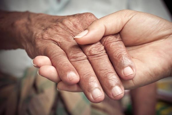 Hands of a caregiver and a senior holding each other