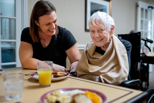 A caregiver smiling with a resident at a dining table