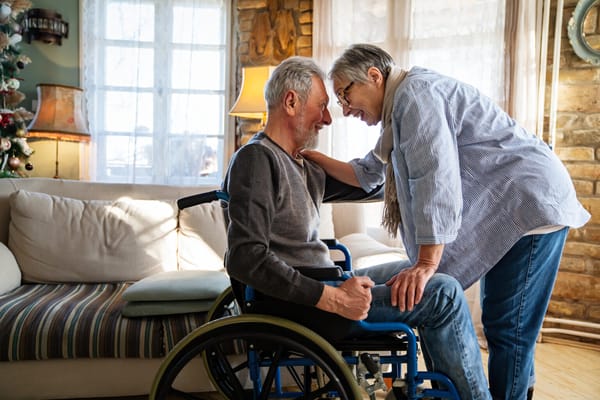 A senior man in a wheelchair interacting with a woman.
