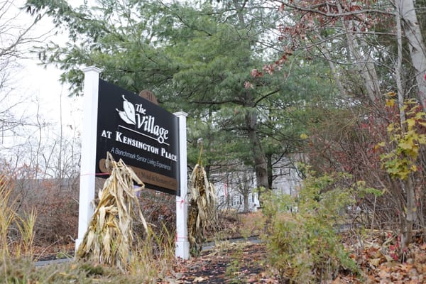 Sign for The Village at Kensington Place surrounded by trees and plants