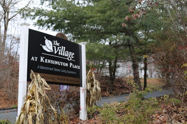 Sign for The Village at Kensington Place in front of a wooded area