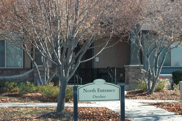 Sign for the North Entrance of Touchmark at Meadow Lake Village with trees in foreground.