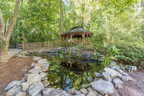 Wooden gazebo next to a pond surrounded by greenery