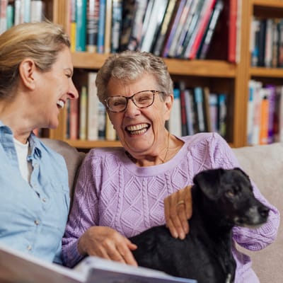 Two women laughing together with a dog in a cozy setting
