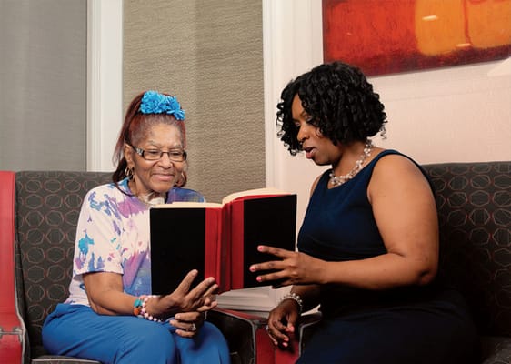 Resident enjoying a book with staff member in a cozy lounge