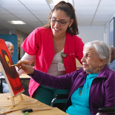 Resident painting with staff assistance in activity room