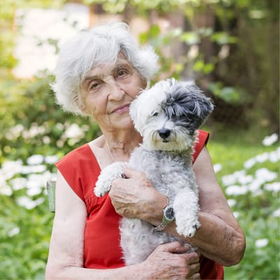 A resident holding a small dog in a garden area