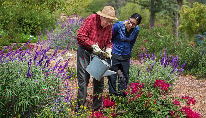 A resident watering flowers with staff assistance in a garden
