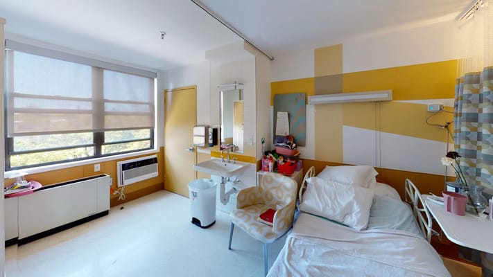 Interior view of a resident room showing a bed, chair, and window.