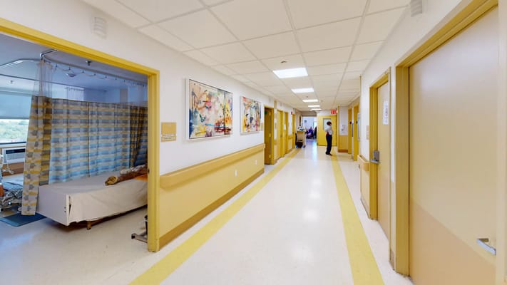 A view of a bright hallway in Laconia Nursing Home with patient rooms on either side.