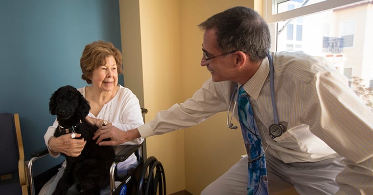 Senior resident smiling with a doctor and a dog