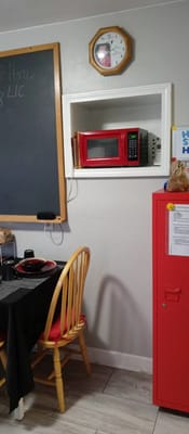 Kitchen area featuring a red microwave, dining table, and clock.