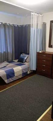 A cozy bedroom featuring a bed with a patterned blanket, a blue pillow, and a wooden dresser.
