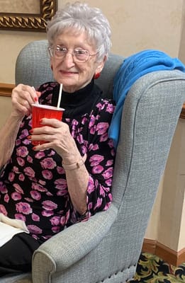 A smiling resident enjoying a drink in an armchair