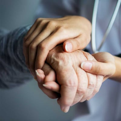 Hands of a caregiver and elderly person clasped together