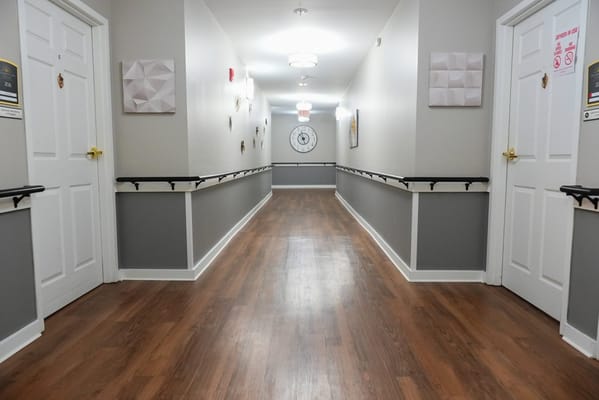 Well-lit hallway with wooden flooring and door signs