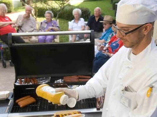 Chef grilling hot dogs for residents in the garden