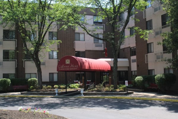 Front entrance with red awning and landscaping at Mayfair Village Retirement Center