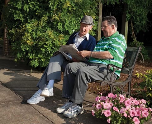Two seniors sitting on a bench reading a newspaper in a garden