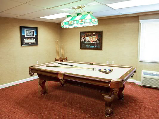 A billiards table in a cozy room with framed pictures on the walls.