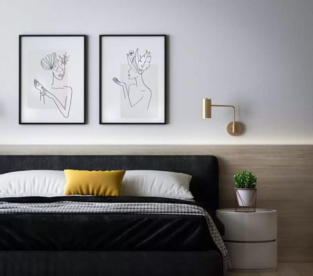 A modern bedroom featuring two line art portraits on the wall above a black bed with yellow accent pillow.