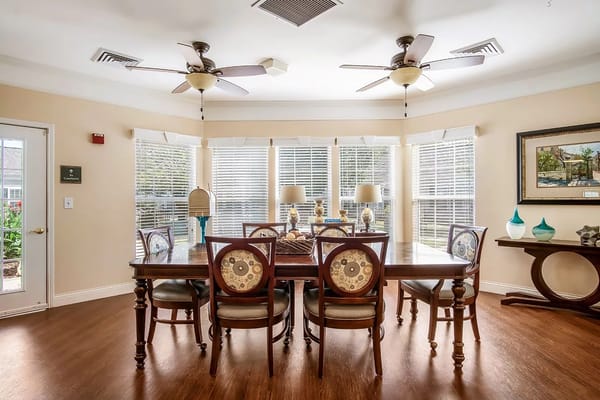 Bright dining area with large windows, a wooden table, and chairs.