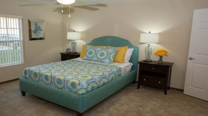 A well-decorated bedroom featuring a teal bed, colorful bedding, and warm lighting.