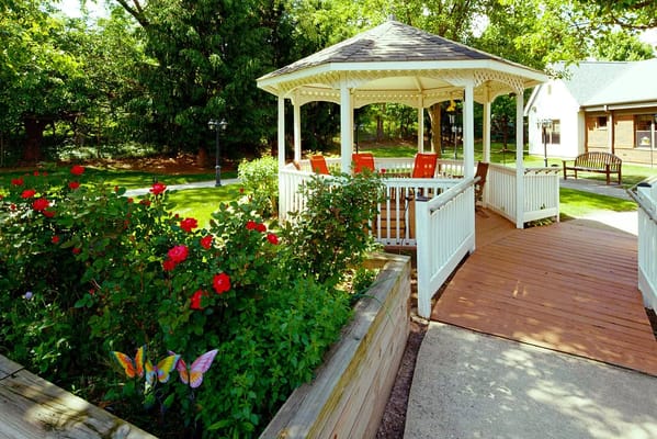 A gazebo surrounded by blooming roses and butterflies in the garden.