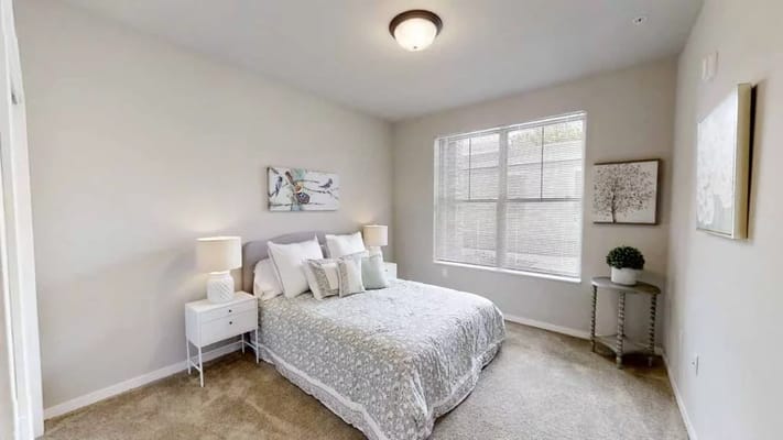 A well-decorated bedroom featuring a large bed, bedside tables, and natural light from a window.