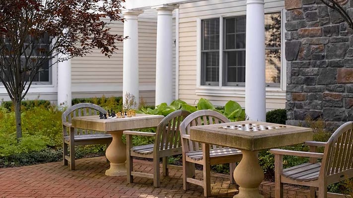 Two stone chess tables with wooden chairs in a landscaped courtyard.