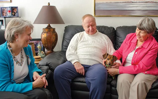 Two elderly residents and a staff member sitting together with a small dog