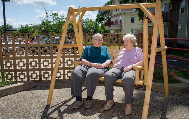 Two seniors sitting on a wooden swing in a garden area.