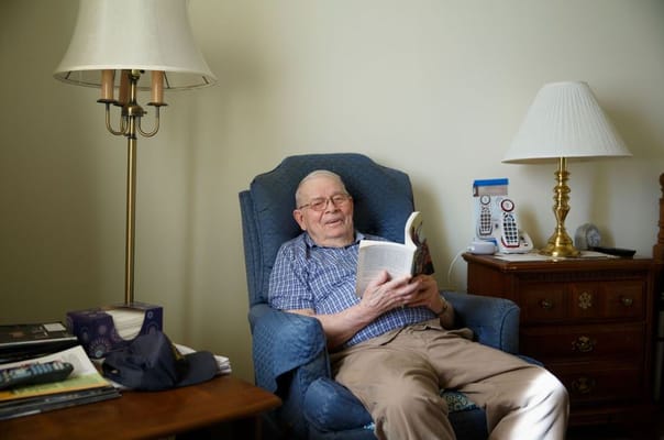 An elderly man reading a book in an armchair