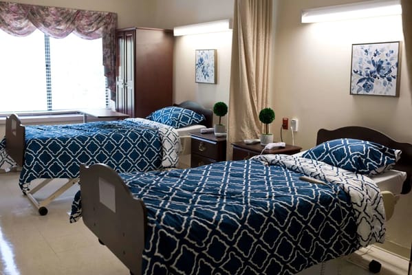 Two beds with blue patterned bedding in a healthcare facility room