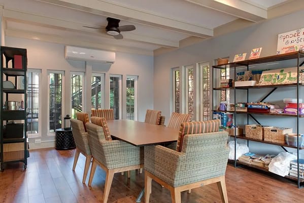 Bright common room featuring a large table and shelves with games and books.