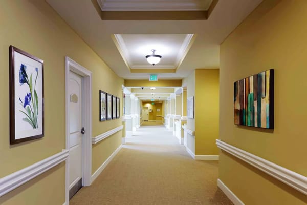 A spacious hallway with framed artwork and yellow walls in Bayshore Memory Care.