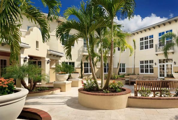 Sunny courtyard with palm trees and flower planters at Bayshore Memory Care.