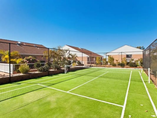 Outdoor tennis court surrounded by gardens and buildings