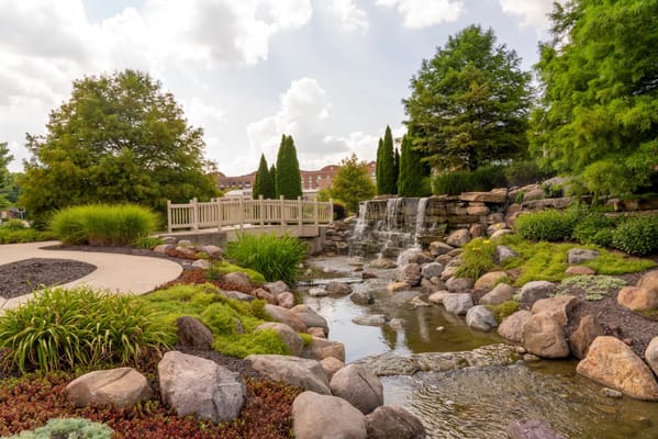 A serene waterfall flowing into a landscaped garden with a bridge.