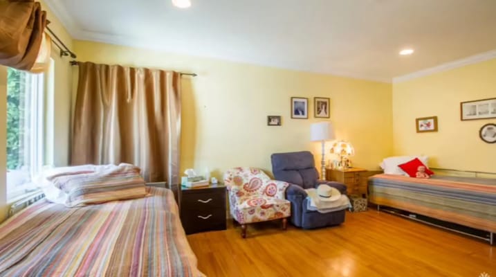 A cozy bedroom with two beds and a chair, featuring warm yellow walls.
